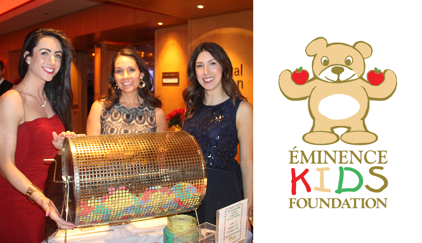 A photo of three women standing behind a prize raffle drum filled with draw entries next to the Eminence Kids Foundation logo.  